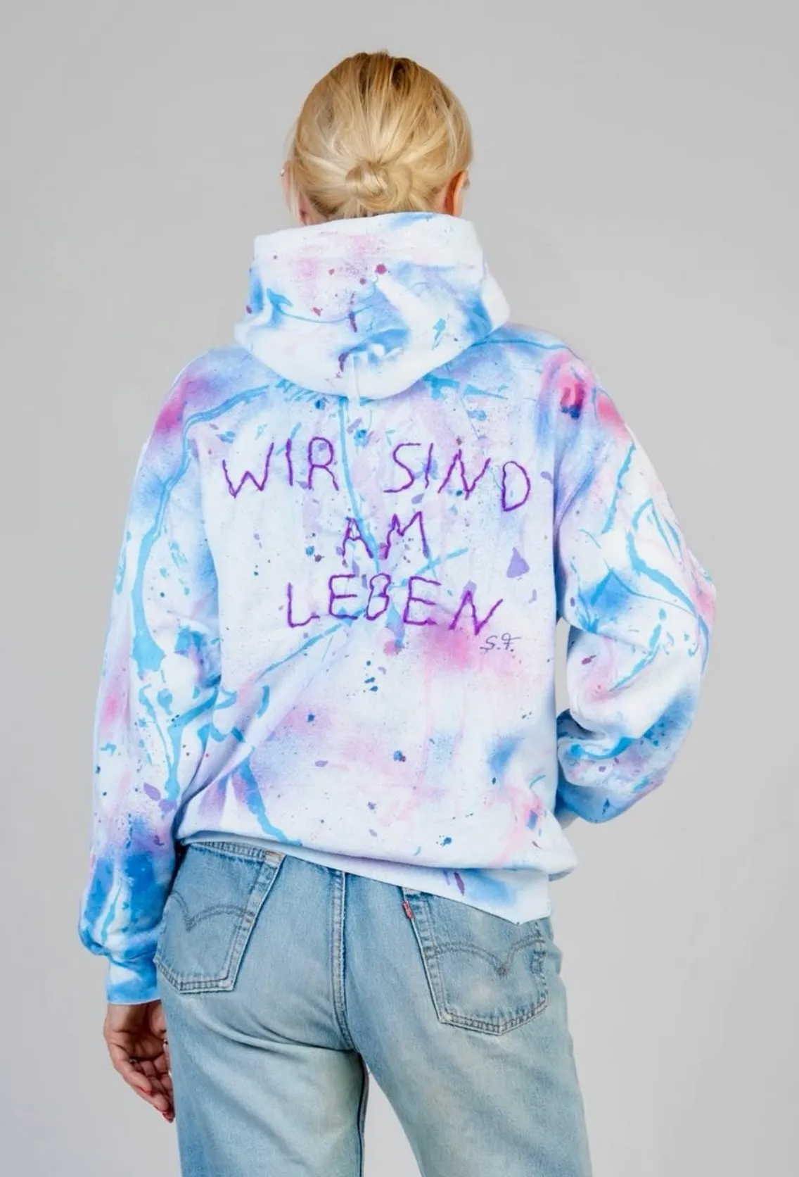 Rückseite eines Unikat-Pullovers mit handgemaltem Schriftzug „Wir sind am Leben“, signiert S.F.